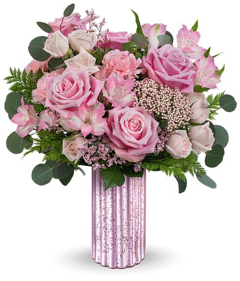 A Mother's Day arrangement featuring light pink spray roses, pink alstroemeria, carnations, limonium, rice flower, and floral greenery in a metallic lavender vase, with a space for a personalized gift message.