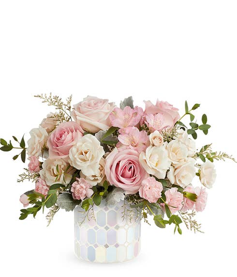 A Mother's Day floral arrangement featuring light pink roses, crme spray roses, light pink alstroemeria, pink miniature carnations, and floral greens, arranged in a white iridescent mosaic vase, with space for a personalized gift message.
