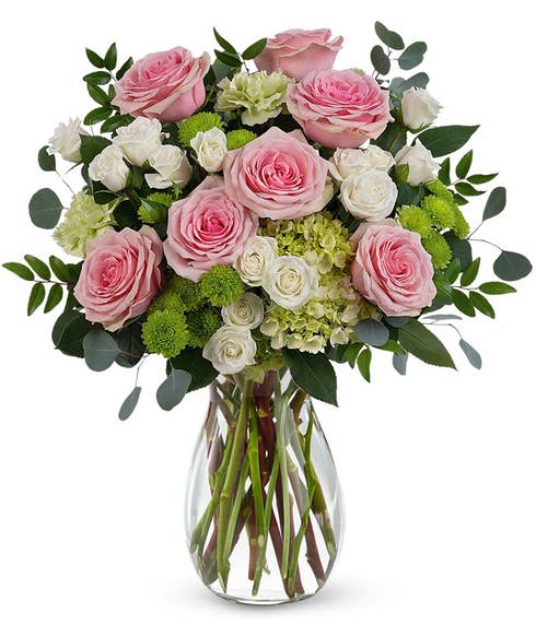 A Mother's Day arrangement featuring green hydrangea, pink roses, white spray roses, green carnations, green button chrysanthemums, and floral greenery, arranged in a keepsake pearl pink swirling vase, with space for a personalized gift mes