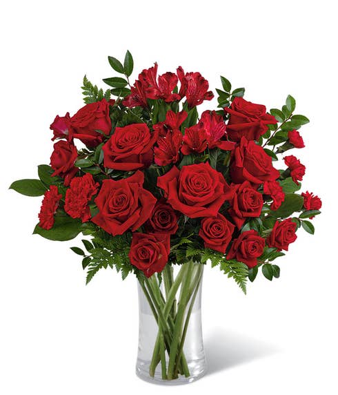Red roses and red spray roses with floral greens in a tall red cylinder glass vase