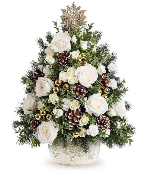 Festive floral arrangement shaped like a Christmas tree, featuring red spray roses, miniature red carnations, white berry accents, and seasonal greenery, topped with a silver snowflake. Displayed in a snowman-shaped container with a red scarf.