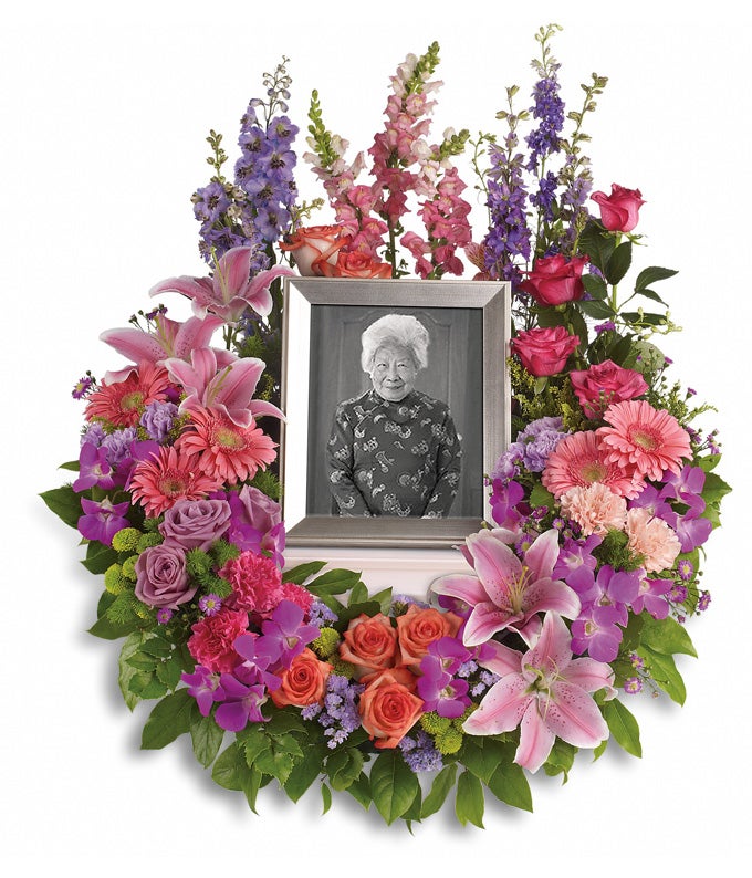 Floral Centerpiece arrangement including Pink And Purple Roses, Hot-Pink Carnations, Light-Pink Gerberas, Blush Oriental Lilies, Pink Snapdragons, Magento Orchids, Violet Asters, Lavender Delphinium, Green Button Spray Chrysanthemums and Lush Greens with picture frame