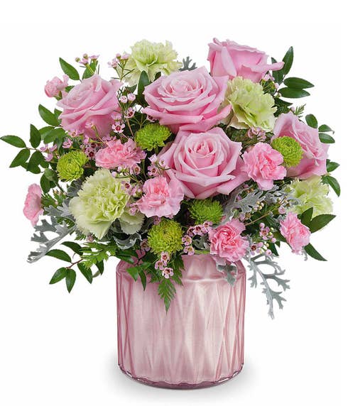 pink roses, green carnations, miniature pink carnations, green button spray chrysanthemums, pink waxflower, and floral greenery in a pink vase.