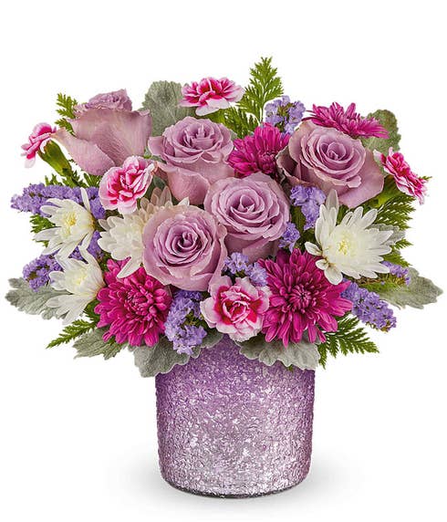 lavender roses, miniature variegated purple carnations, purple cushion spray mums, white cushion spray mums, and floral greenery in a sparkling purple vase.