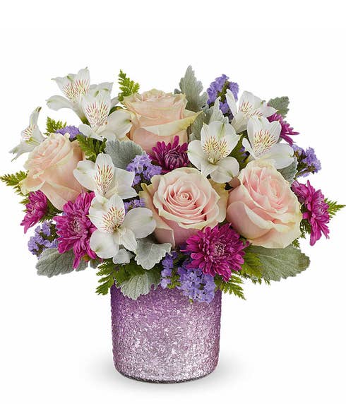 pink roses, white alstroemeria, purple cushion spray chrysanthemums, lavender sinuata statice, and floral greenery in a sparkling purple vase.
