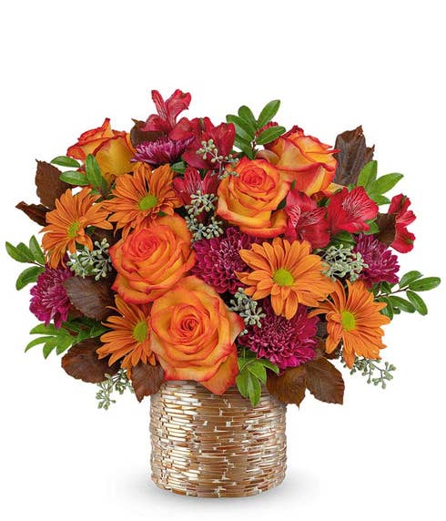 Fall flower arrangement with orange and yellow bi-color roses, red alstroemeria, orange daisy poms, burgundy button spray chrysanthemums, and greenery in a gold-glass textured vase.