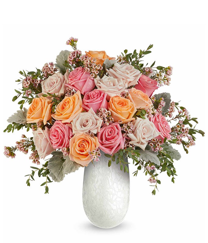 Light pink roses, peach roses, pink roses, and floral greenery in a tall white pearlescent vase