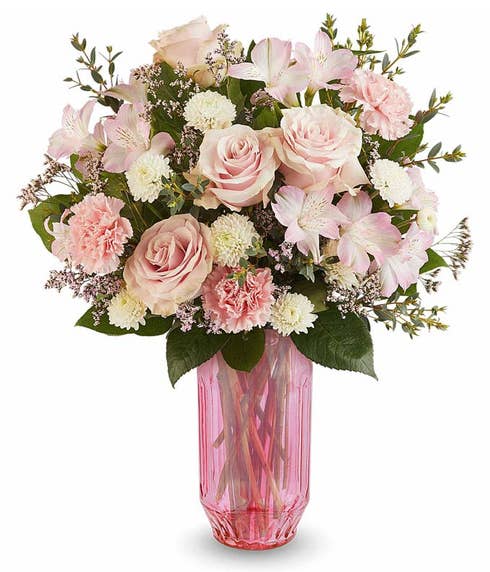 Hot pink roses with pink spray roses, alstroemeria, miniature pink carnations, and greenery arranged in a blush pink glass vase