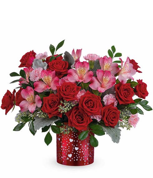 Red roses with pink alstroemeria, pink carnations, and lush greenery arranged in a red lantern-style vase with heart cutouts