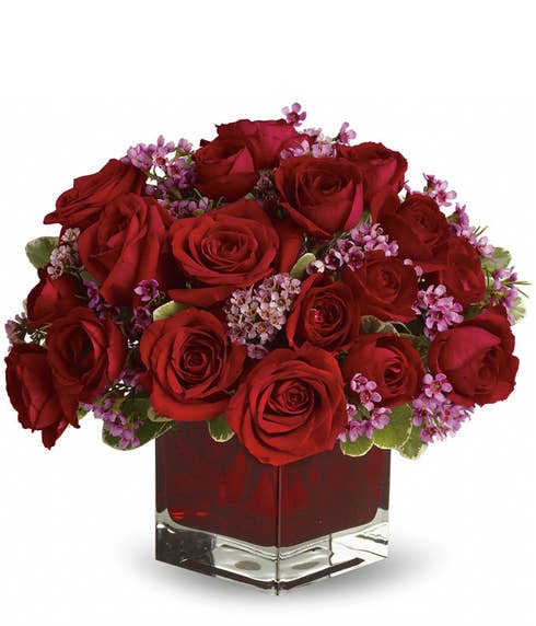 Romantic red roses and purple waxflower bouquet in a square dark red glass vase