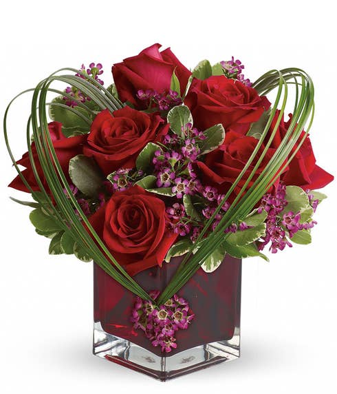 Modern heart shaped red roses and purple waxflower bouquet in red square vase