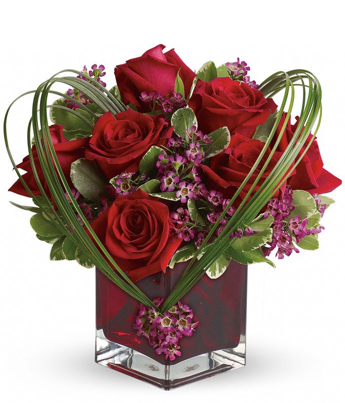 A Bouquet of Red Roses, Purple Waxflower, Variegated Pittosporum, and Bear Grass in a  Glass Scarlet Colored Vase