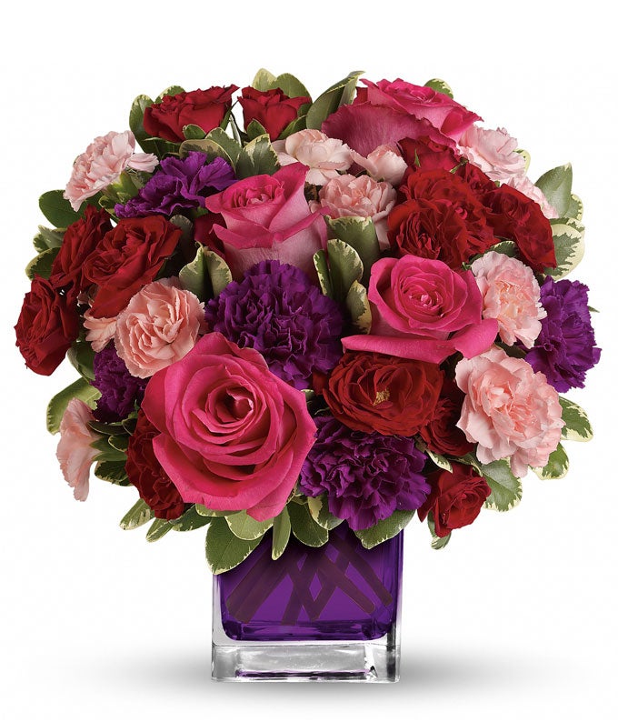 A Bouquet of Hot Pink Roses, Dark Red Spray Roses, Purple Carnations, and Pink Mini Carnations in a Violet Glass Cube Vase