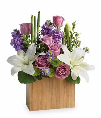 A bouquet of  Lavender Roses, White Asiatic Lilies, Lavender Stock, Monté Cassino Asters, Green Chrysanthemums and Fresh Greenery in a Bamboo Vase