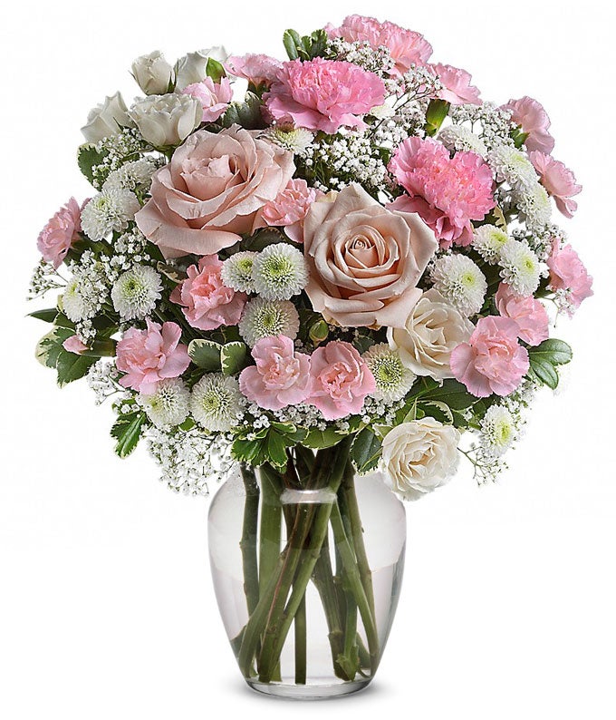 A Bouquet of Pink Roses included in deluxe and premium Arrangement only, Pink Carnations, White Button Spray Mums, Million Gypsophila, and Lush Greens in a Clear Vase