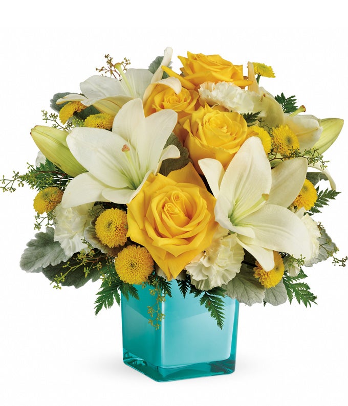 A Bouquet of Deep Yellow Roses, Asiatic Alabaster Lilies, Pale Cream Carnations, Canary Chrysanthemums Button Spray, Seeded Eucalyptus, Dusty Miller, and Leatherleaf Fern in a Cube Turquoise Vase