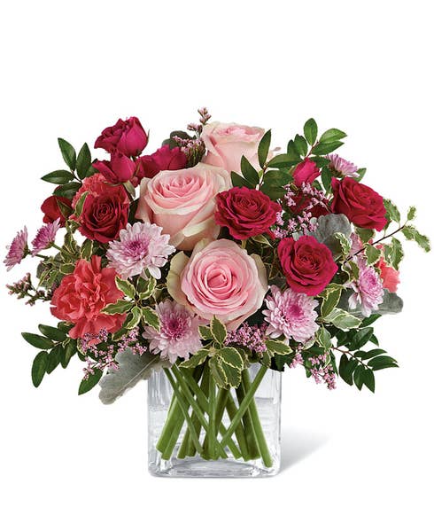Pale pink roses, red roses, pink chrysanthemums and peach carnations in a pink vase