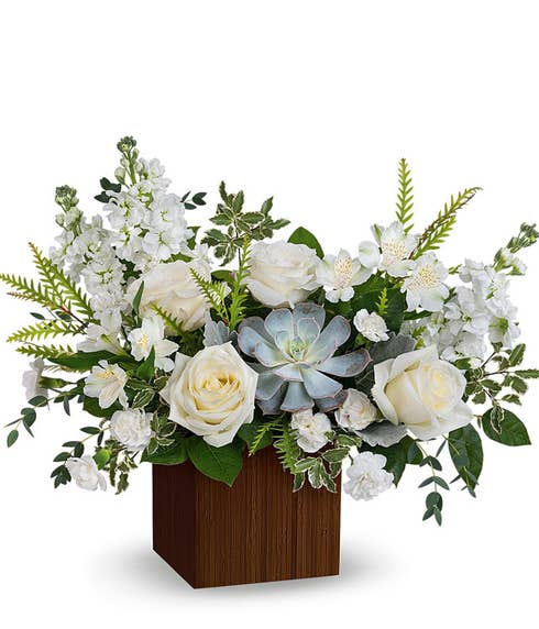 White roses, white alstroemeria, white mini carnations, white stock, echeveria succulent, and floral greens in a brown bamboo cube vase 