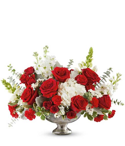 Red roses accented with white blooms, red carnations, and lush greenery arranged in a classic silver pedestal bowl