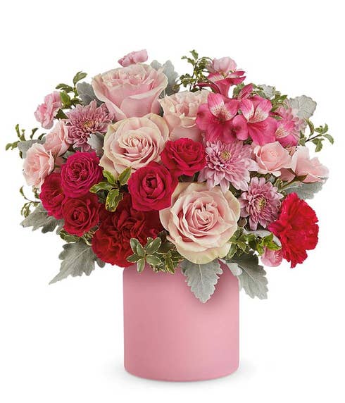 Pink and red roses with pink carnations, alstroemeria, and lush greenery arranged in a modern pink savannah jarvase