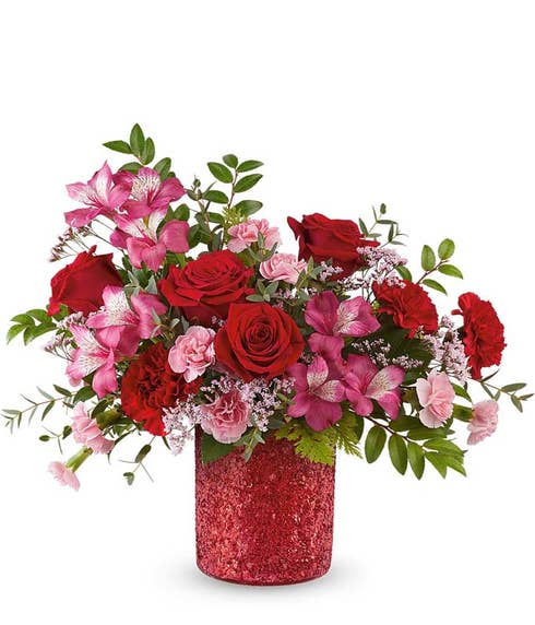 Red roses with pink alstroemeria, red and pink carnations, and lush greenery arranged in a glittered red cylinder vase