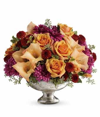 A Bouquet of  Lush Greens, Orange Roses, Gladioli, Lavender Cushion Spray Mums, Orange Lilies and 1 Orange Candle in a Mercury Glass Vase